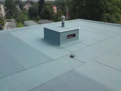 Roh ploché střechy s boxem, v pozadí rodinné domy