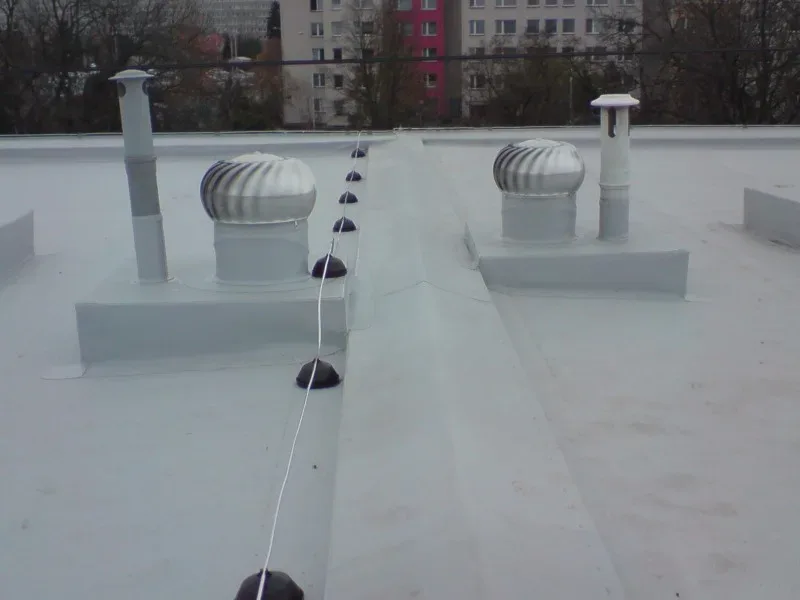 Dvě rotační ventilační hlavice na ploché střeše s bezpečnostním lanem, slunečný den