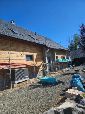 Sedlová střecha s tmavou skládanou krytinou a třemi střešními okny nad fasádou s dřevěným obkladem, podél domu lešení
