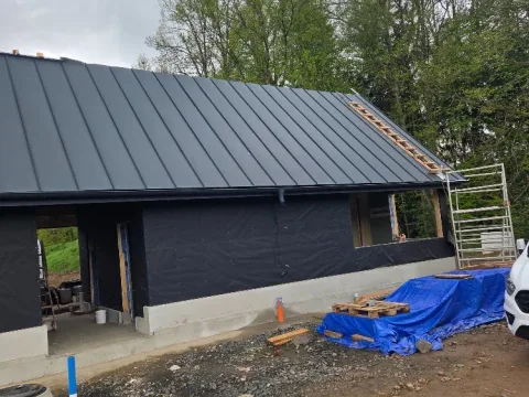 Druhá část novostavby se sedlovou střechou z tmavého plechu na stojatou drážku, u štítu lešení a zakrytý stavební materiál